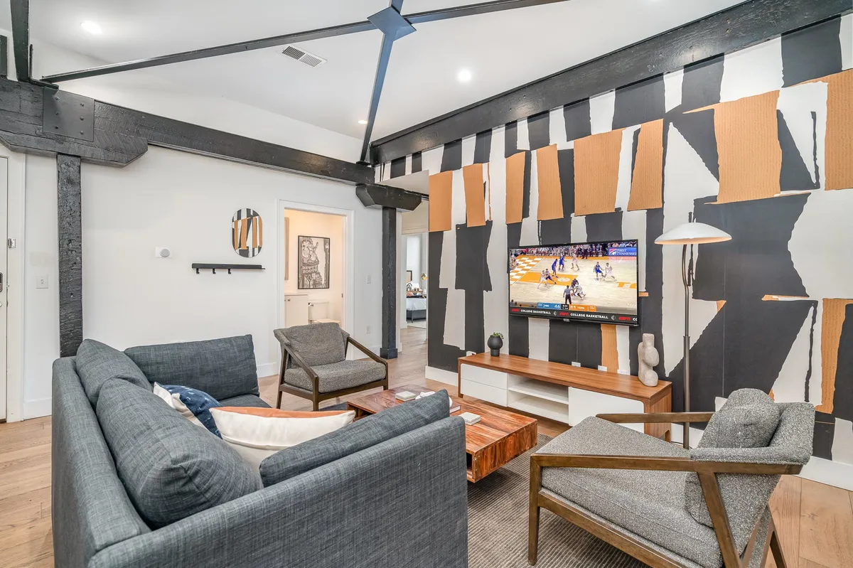 A lively living space with an abstract wall art backdrop, a wooden coffee table, a modern sofa, and a television broadcasting a sports event. The stylish floor lamp and overall setup suggest a perfect spot for group conversations, watching the big game, or entertaining guests.