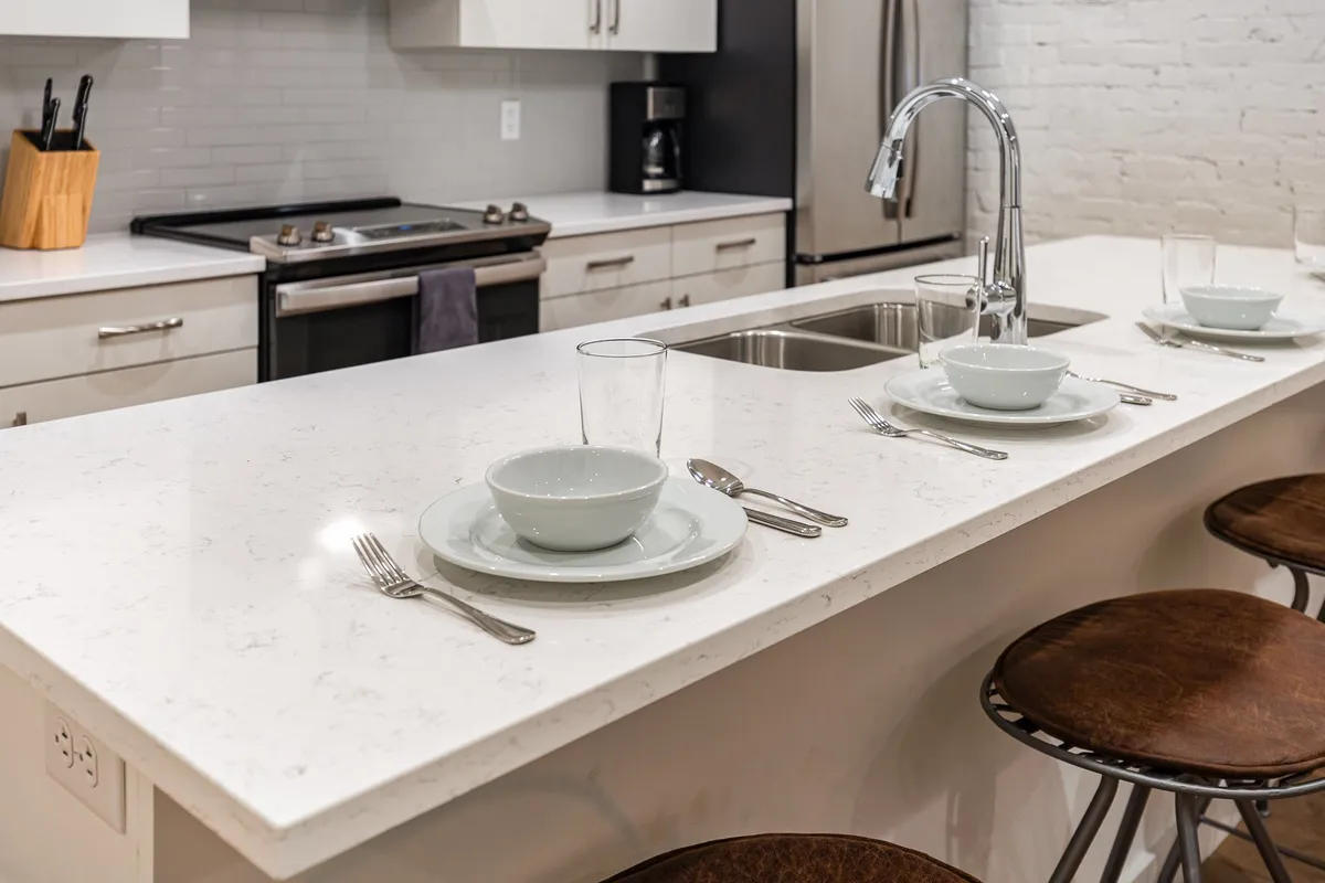 A cozy, inviting kitchen scene featuring a spacious kitchen island with stools, gleaming stainless steel appliances, and dinnerware set out for entertaining. The warm ambiance is enhanced by guests engaging in cooking and casual dining, suggesting a lively, communal atmosphere.