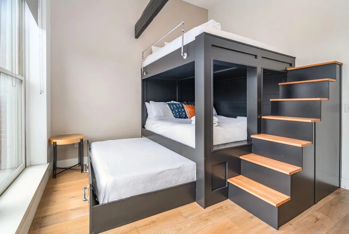 A playful bedroom centered around a king-over-king bunk bed structure, complete with a staircase for easy access and a nightstand beside the bed. The mood is inviting and fun, offering unique sleeping arrangements perfect for groups or families.
