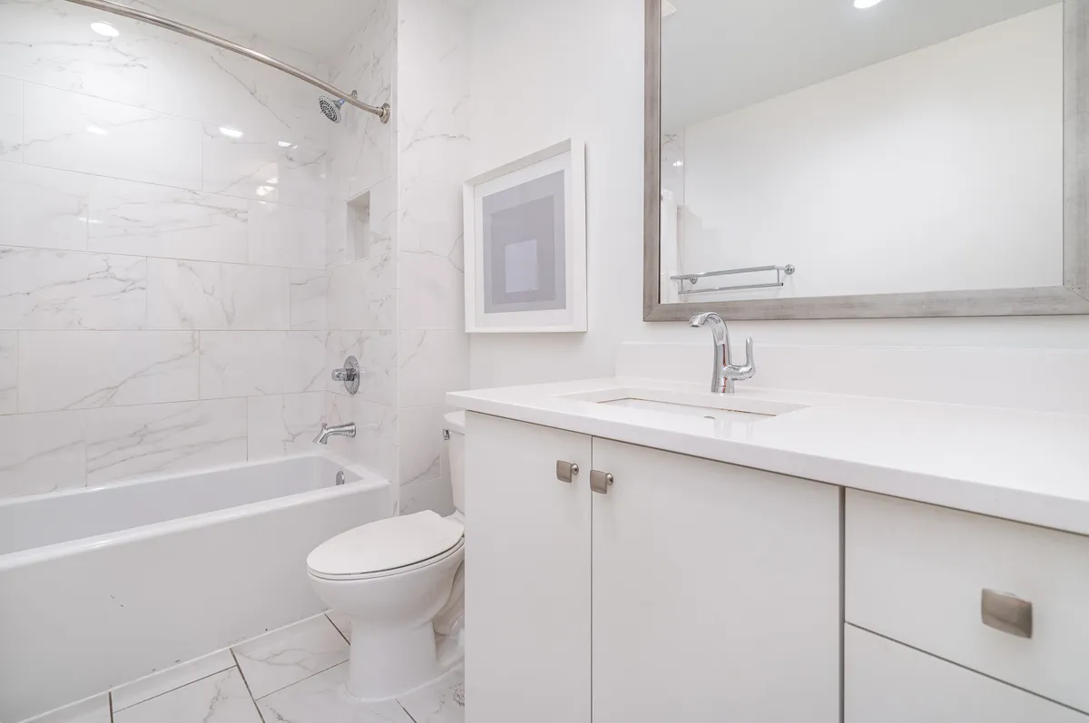 A serene bathroom setting with white marble tiles, a modern vanity, framed artwork, and a spacious shower area that exudes elegance and relaxation.
