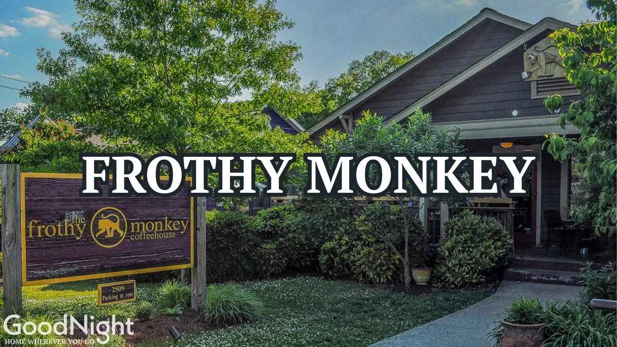 An inviting exterior shot of Frothy Monkey shows its distinctive signage, entrance pathway, and lush surrounding greenery. Outdoor seating is visible, suggesting a welcoming atmosphere for morning coffee and casual gatherings.